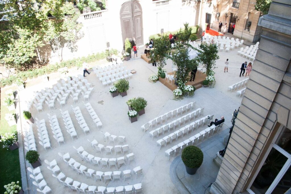 Cérémonie aménagée dans une cour avec chaises blanches et décor végétal, Mariage dans l’Air