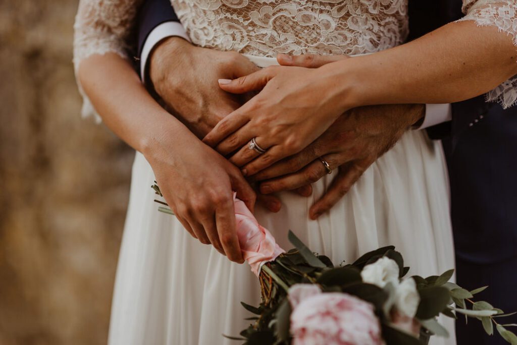 Gros plan sur les mains des mariés et leur bouquet
