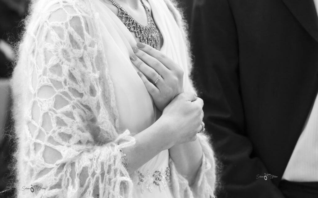 Détail en noir et blanc d’une mariée en dentelle près d’un homme en costume — Solenne Ottmann Photographe
