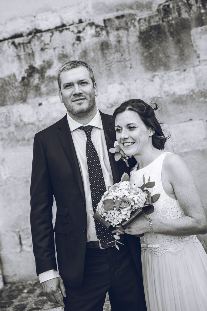 Portrait en noir et blanc d’une mariée souriante avec son bouquet, auprès du marié