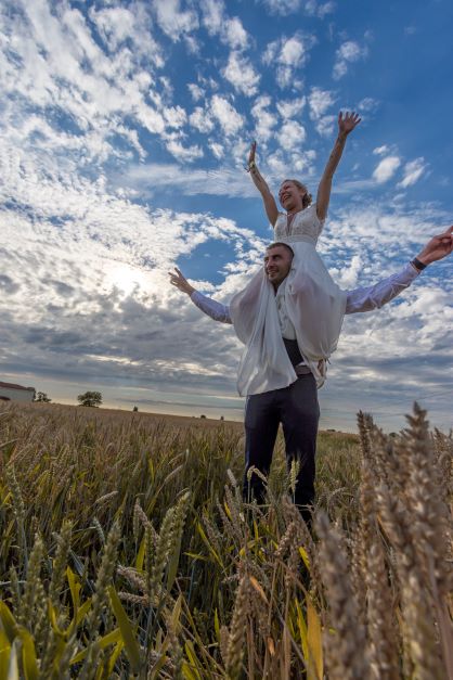 Mariée portée sur les épaules du marié dans un champ sous un ciel nuageux