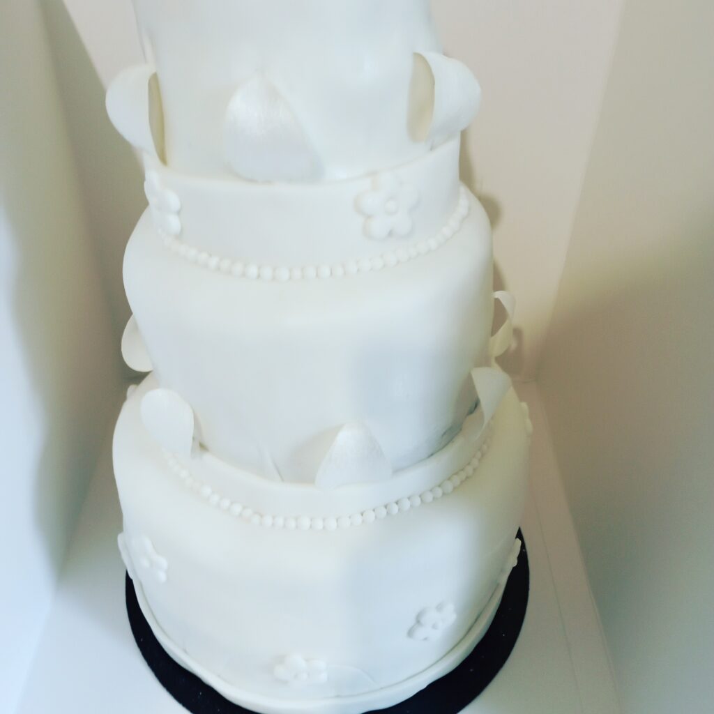 Détail d’un gâteau blanc à étages avec nœuds et perles décoratives