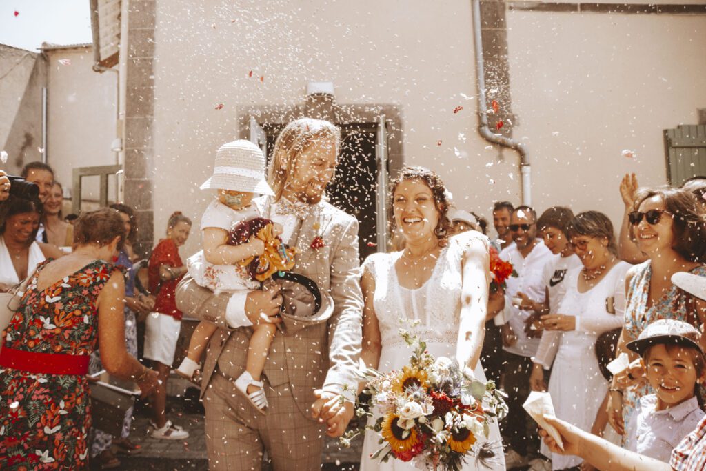 Mariés avec un enfant sous une pluie de confettis à la sortie de la cérémonie