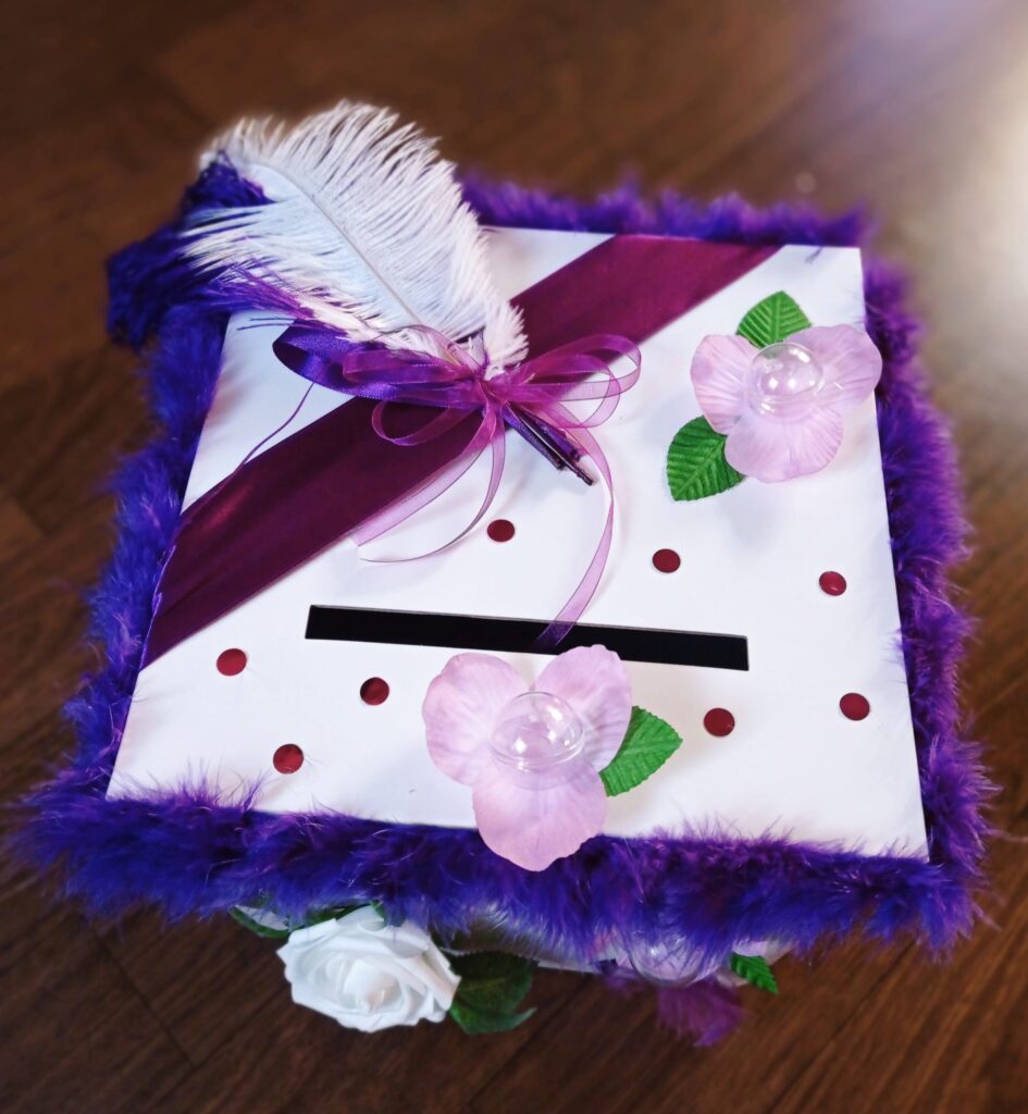 Urne blanche décorée de plumes violettes, de rubans et de fleurs roses