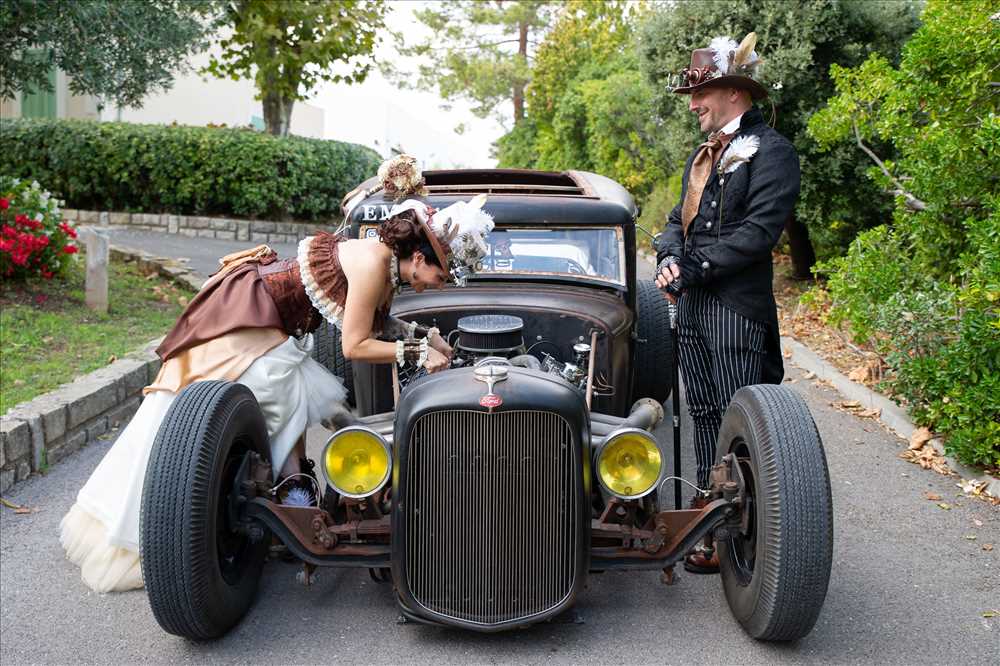 Couple en tenues de mariage rétro près d’une voiture ancienne au moteur découvert