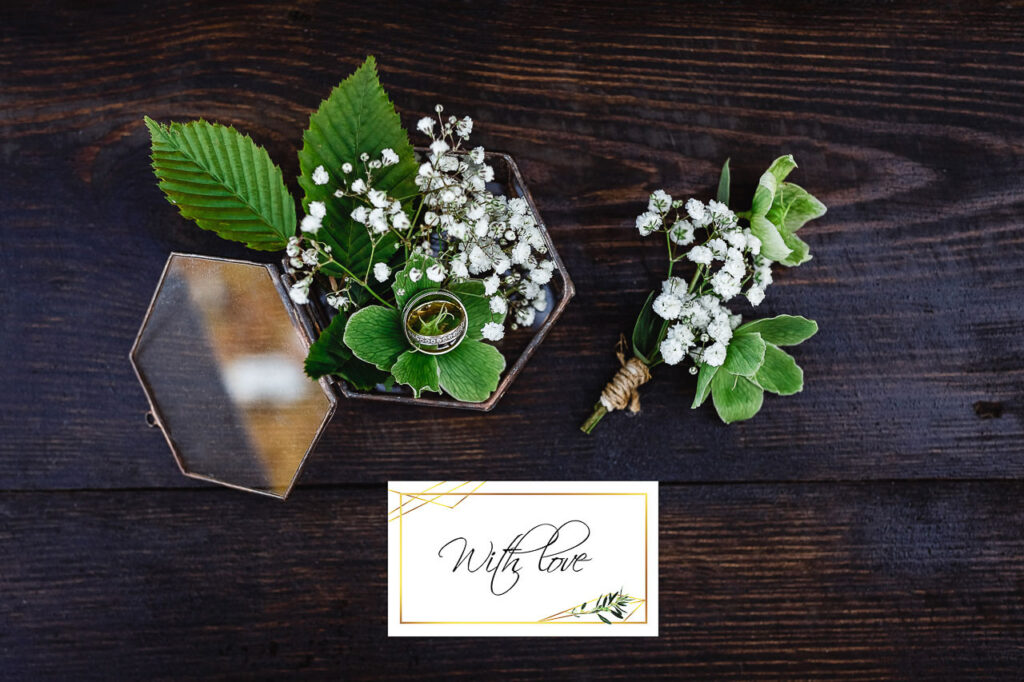 Alliances dans une boîte en verre avec feuillage et petites fleurs blanches