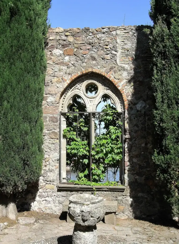 Gothic stone opening framed by cypress trees in the garden of Château de La Napoule