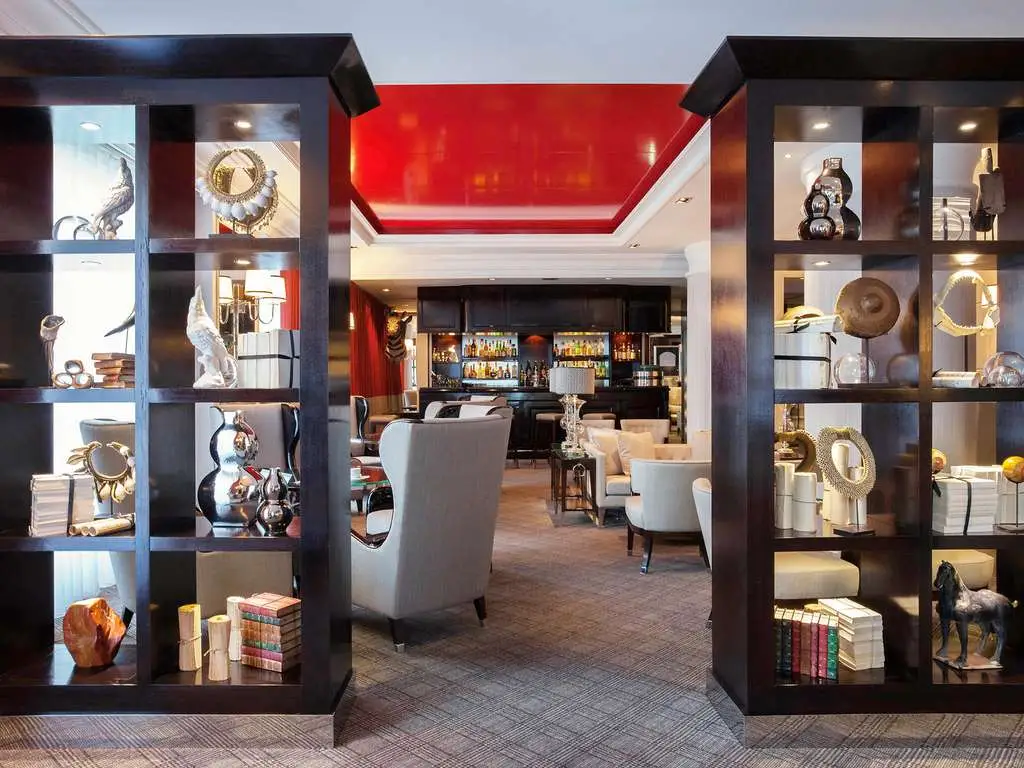 Espace lounge du Park Hôtel Grenoble avec fauteuils, bibliothèque décorative et plafond rouge