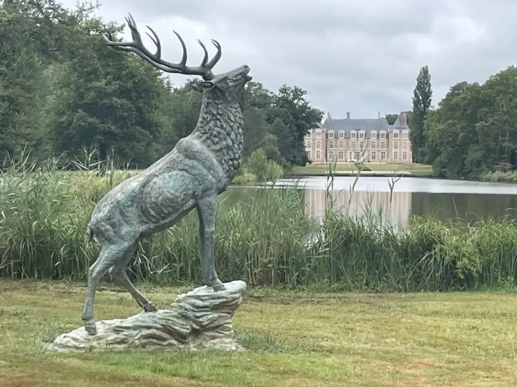Château de La Borde derrière la pièce d’eau, avec une statue de cerf au premier plan