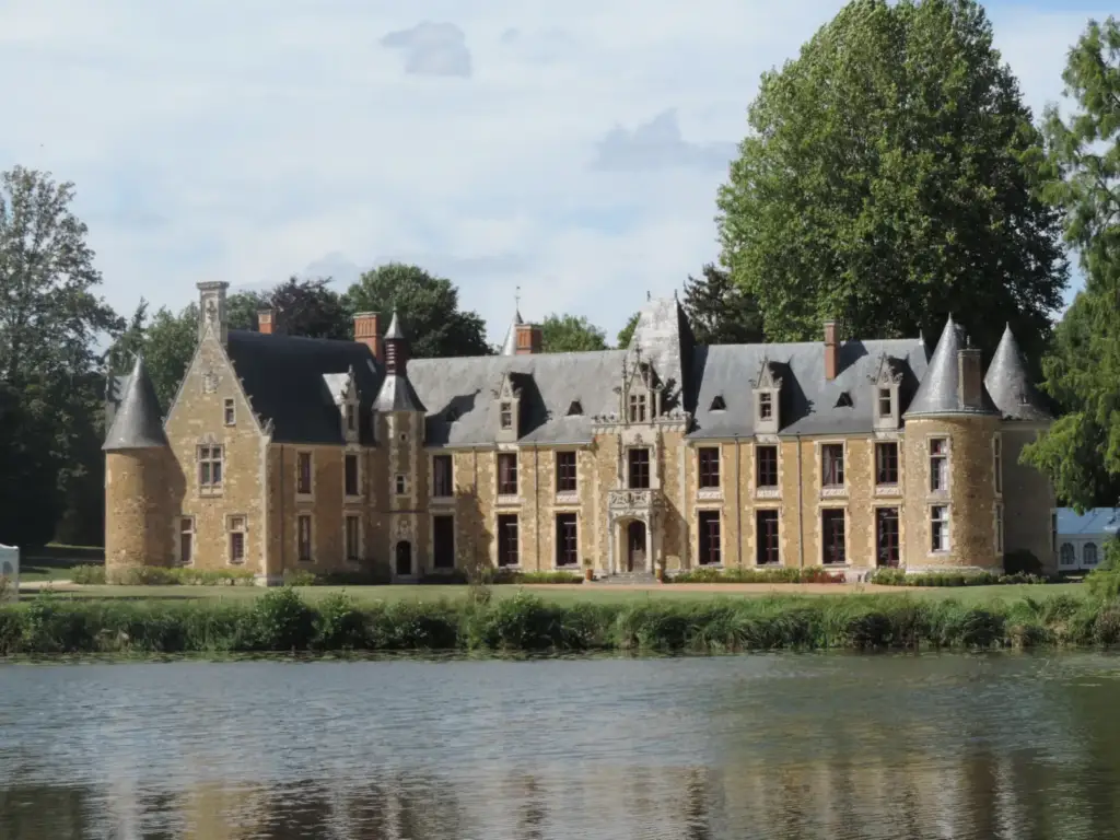 Façade en pierre et tours du Château de Chéronne derrière la pièce d’eau