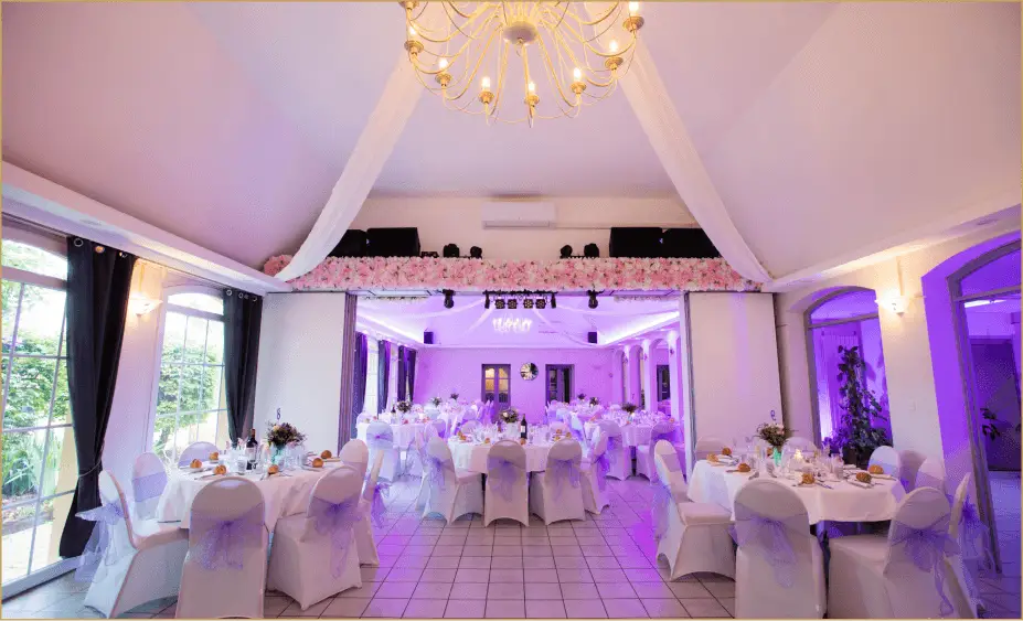 Salon de réception du Château de la Baume avec tables rondes, voilages blancs et éclairage mauve