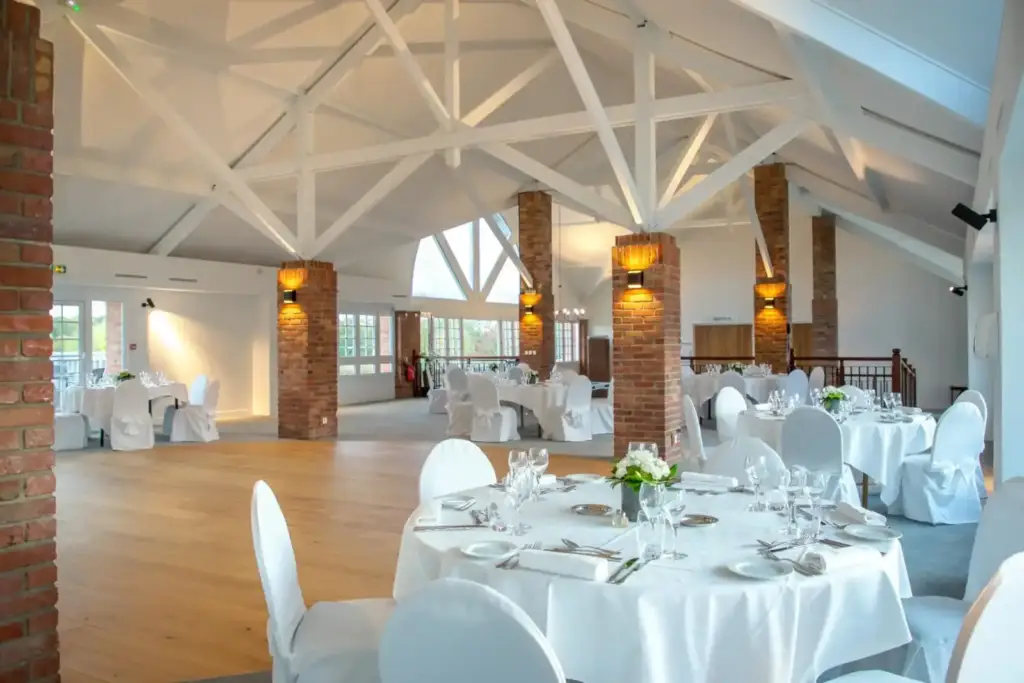 Tables de réception sous la charpente blanche et entre les piliers en brique du salon Par en Par au Mercure Chantilly
