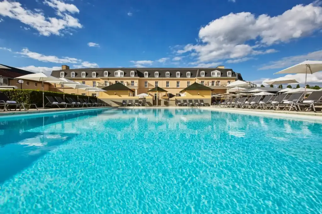 Piscine extérieure du Mercure Chantilly avec la façade de l’hôtel, des transats et des parasols