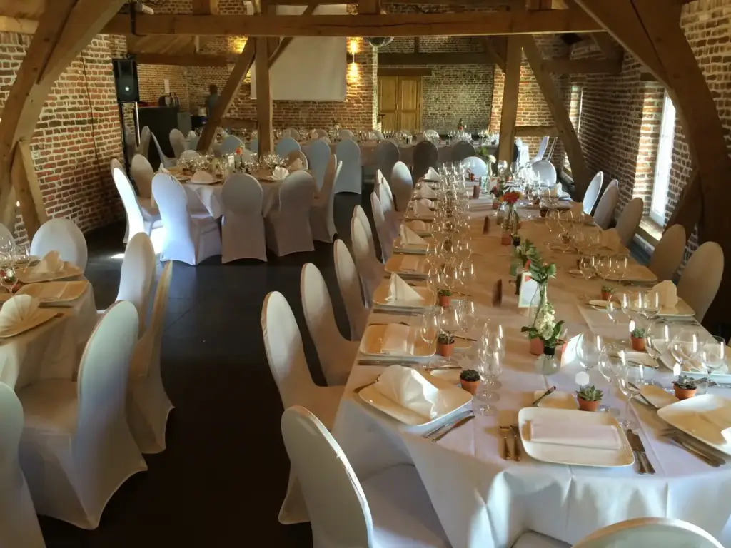 Salle de banquet de la Ferme du Château d’Oudoumont avec poutres apparentes et tables dressées