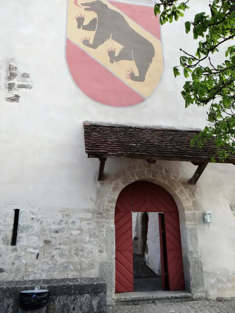 Red entrance door at Schloss Laupen beneath the Bern coat of arms and a tiled canopy