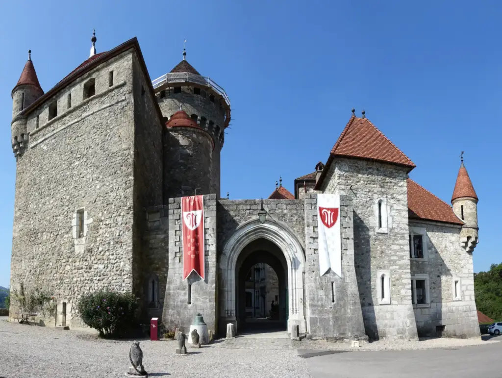 Entrée voûtée et tours en pierre du Château de Montrottier, avec deux bannières rouges et blanches