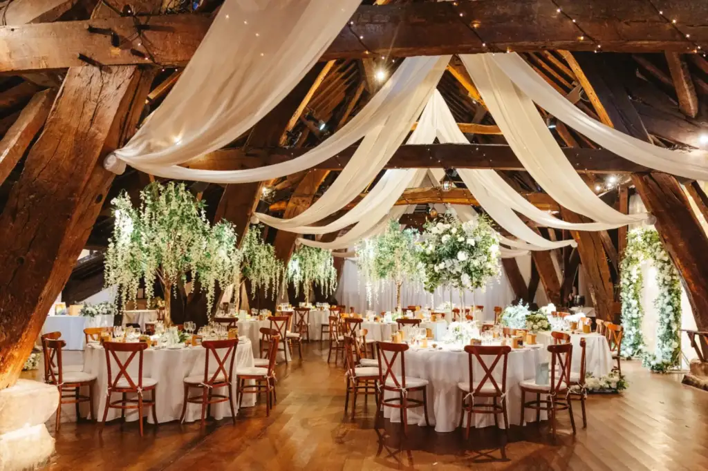Wedding reception tables beneath timber beams and draped fabric at Rivington Hall Barn