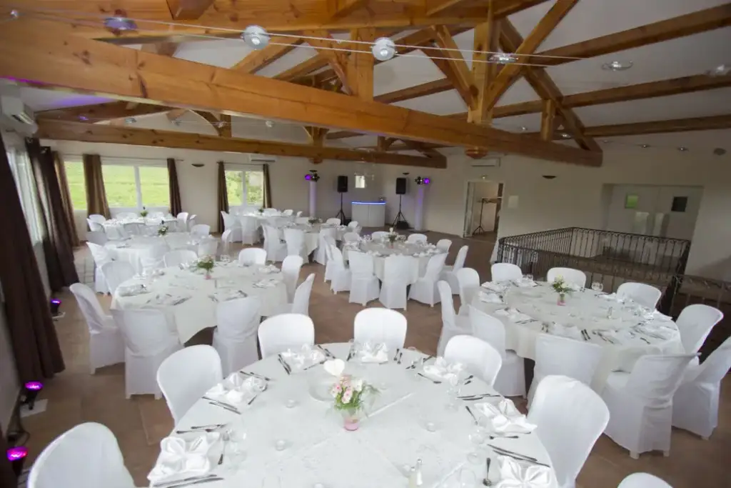 Salle de réception du Domaine de Sigalous avec charpente apparente et tables rondes dressées
