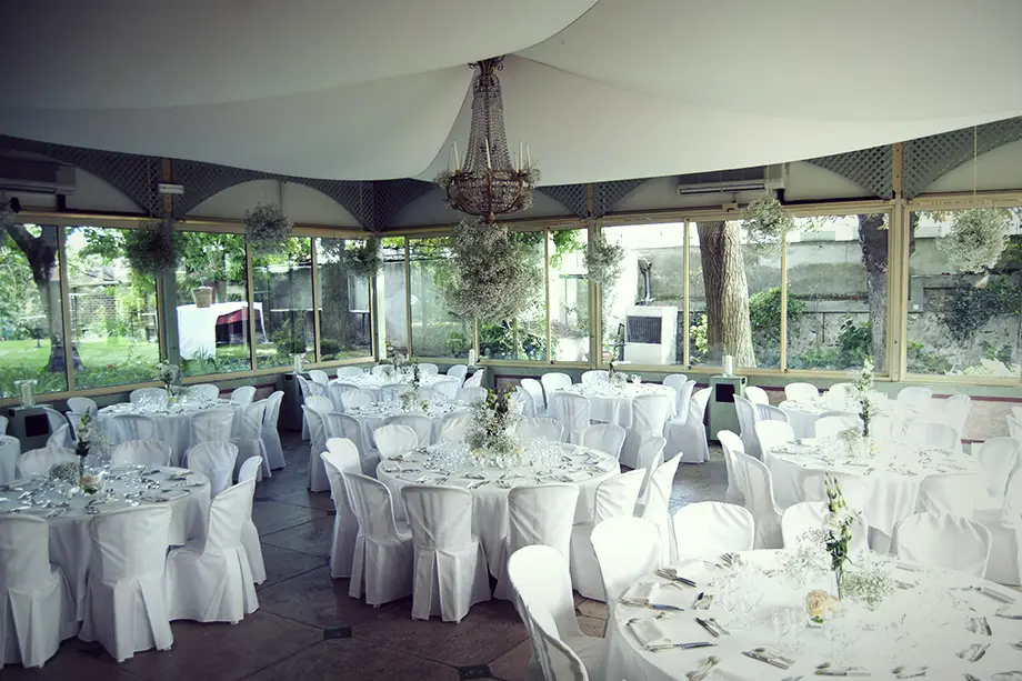 Véranda des Érables avec tables rondes dressées pour une réception et vue sur le jardin